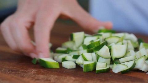 Female chef's hands cut zucchini on wooden cutting board. Summer healthy vegan vegetables salad.