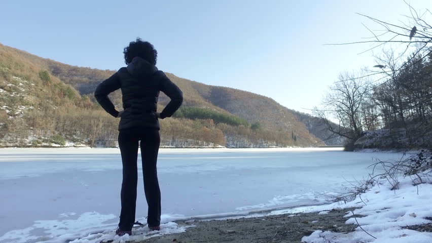 Happy woman in victory pose hands open standing on edge of frozen lake