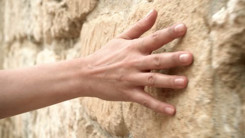Woman's hand moving over old stone wall. Sliding along. Sensual touching. Hard stone surface.