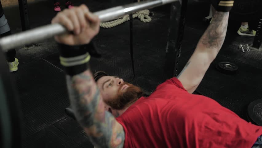 Close up portrait of a concentrated bearded sports man doing squatting exercises with barbell in crossfit center