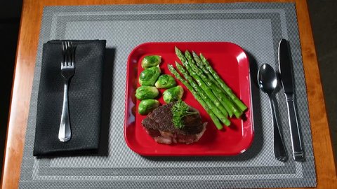 A low-carbohydrate meal of steak, brussels sprouts and asparagus is served on a red plate, which is placed on a gray place mat