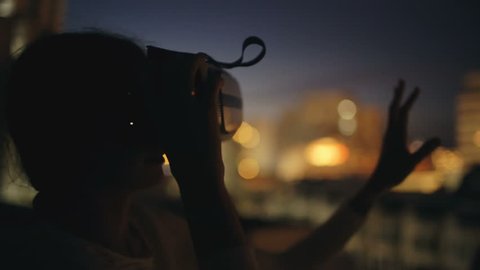 Young woman on rooftop terrace using virtual reality headset and having VR experience at night