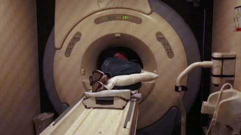 Hospital emergency MRI on man patient. View through protective screen window. Man lays in Magnetic Resonance Image device to look deep into soft muscles and bones. Injury diagnostic before surgery.