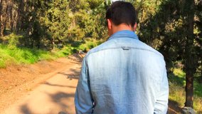 Video of young handsome man in jeans shirts jogging alone in a sunny woods. 