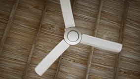 White. plastic fan with three blades spins very slowly as it hangs from a plain. wooden ceiling. UltraHD 4k footage