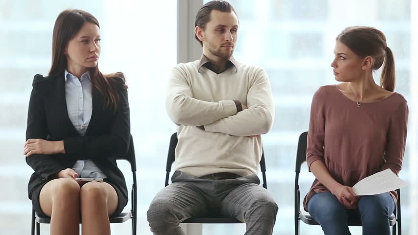 Group of three young applicants sitting on chairs in modern office lobby, waiting for job interview, feeling nervous. Funny rivals looking at each other with arrogant face expressions. Job search Royalty-Free Stock Footage #25331168