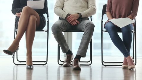 Ready to get new career. Group of three young businesspeople sitting on chairs in office, waiting and going for job interview, feeling nervous. Body language. Close up of legs. Job search concept