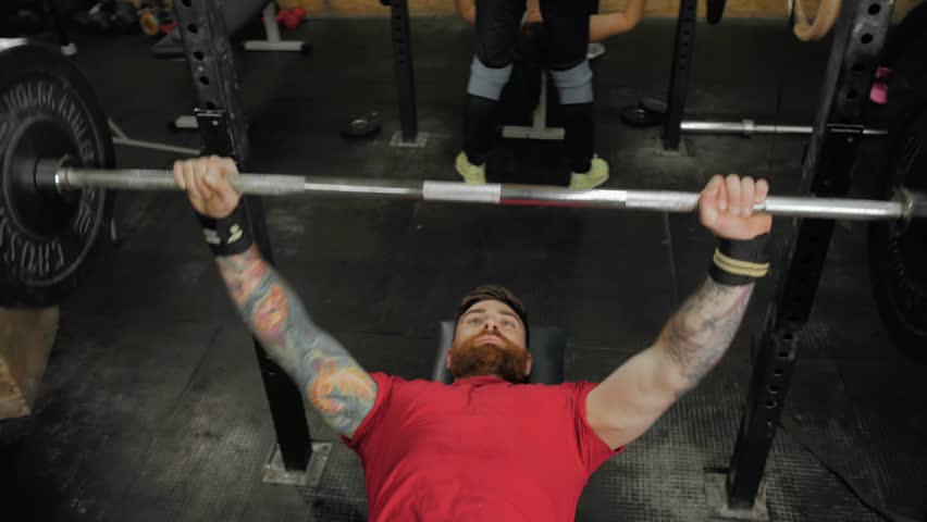 Young man lifting the barbell in the gym portrait. Steadycam follow shot of male athlete with brutal beard