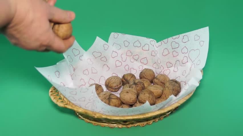 Nuts in a basket impose hands. Green background.