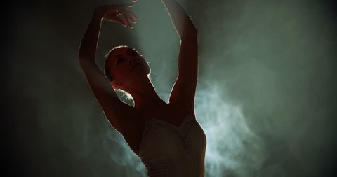graceful ballerina dancing elements of classical ballet in the dark with light and smoke on the background, slow motion