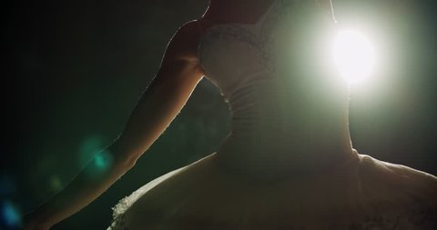 A graceful ballerina dancing ballet elements in the dark with light and smoke on the background, slow motion