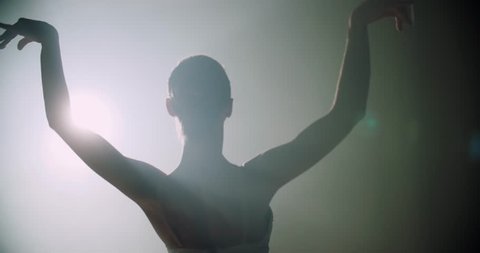 Ballerina dances on stage, close-up with magic light and smoke on the background, slow motion