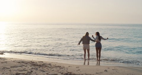 Two young woman arms raised discovering beautiful tropical beach teenager girls enjoying nature together as best friends celebrating summer vacation