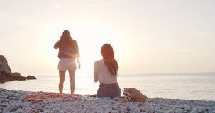Two girl friends taking photograph of sunset on empty beach smartphone women photographing sunrise scenic landscape nature background view enjoying vacation travel adventure
