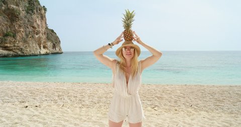 Happy woman balancing pineapple on head posing for camera being silly and playful on tropical beach summer vacation holiday 스톡 비디오