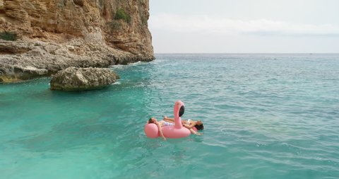 Two girls lying on inflatable flamingo Best friends having fun relaxing floating in clear blue ocean Happy Women enjoying summer vacation on tropical island holiday