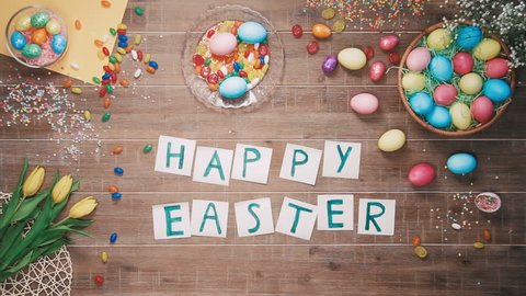 Man put words Happy Easter on table decorated with easter eggs. Top view