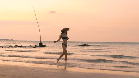 Slow motion of happy woman in hat running on beach during sunset on vacation