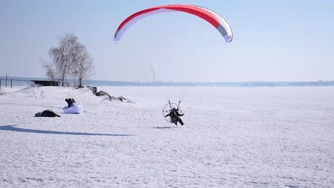 A male athlete flies across the sky on a paraglider, in winter, makes a landing on the snow. 4k. 3840x2160