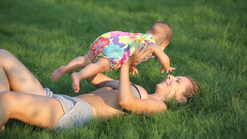 young girl lying in the deep grass and holding her baby under belly