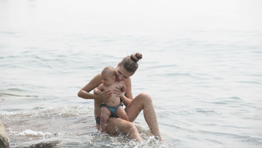 young mom with small child sitting on the rock dangling their legs in the water
