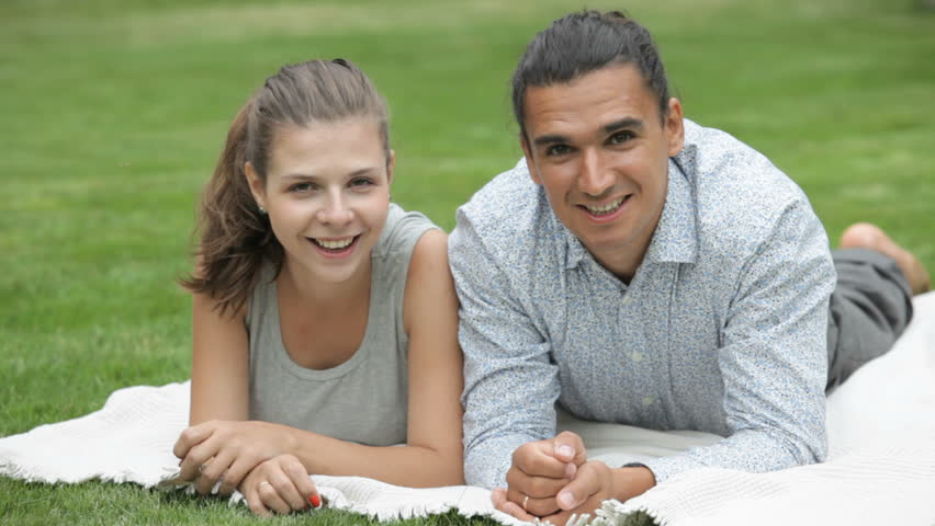 young girl and guy lying on the meadow smiling and looking to the camera