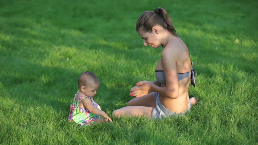 young woman playing with her little child in the fresh green grass