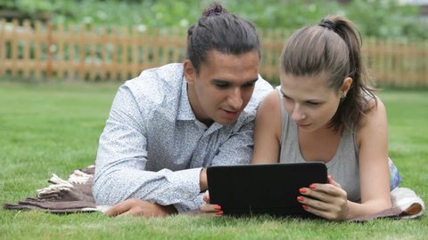 beautiful guy and girl lying on the grass and watching on the e-book