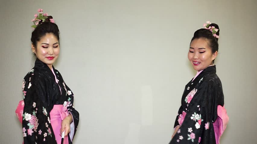two beautiful geishas in a traditional japanese kimono smiling and twisting parasols