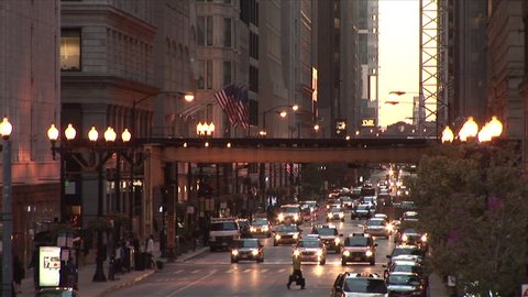 Chicago, IL - CIRCA September 2007: A busy street scene with an elevated train passing through the frame with traffic coming towards the camera at dusk Stock Video