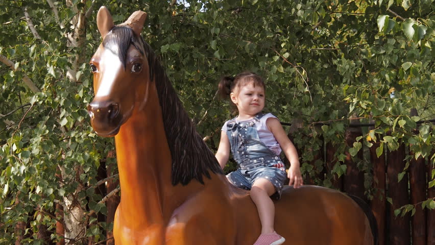The child is playing on the playground. Little girl is sitting on a toy horse. Beautiful little girl is playing in the park. Slow motion.