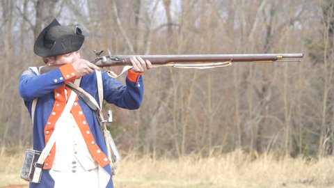 VIRGINIA - OCTOBER 2016 - American Revolution era Continental U.S. Soldier. Re-enactors, reenactment.  Firing Brown Bess musket gun with black powder and lead bullets in earthen fort in battle. 
