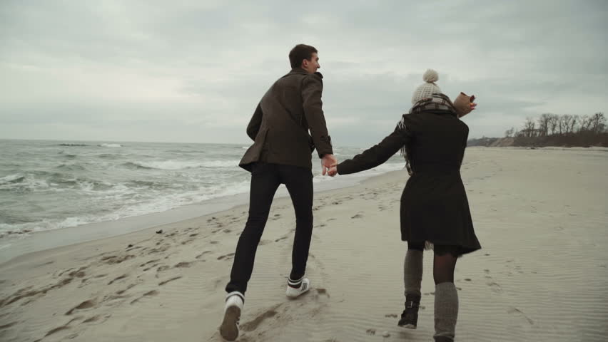 Young couple Run on the beach at the sea, walking the beach, coat and hat, Baltic or Iceland cold weather. 3 axis stabilizer shot