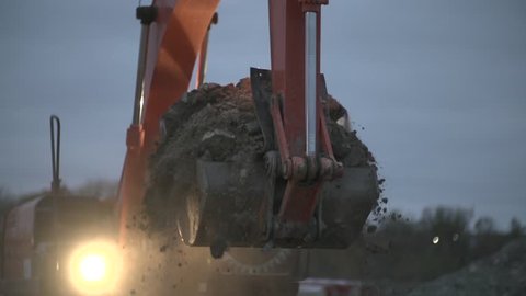 Excavator transports ground at night.Soil falling out of scoop. Construction excavator digging in the ground at construction or job site. Slow motion shot.Heavy machinery,industrial equipment concept.