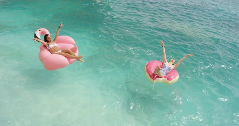 Two girls lying on inflatable flamingo Best friends having fun relaxing floating in clear blue ocean Happy Women enjoying summer vacation on tropical island holiday.