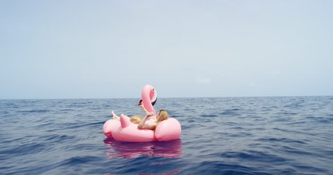 Woman lying on pink inflatable flamingo taking selfie photograph floating alone in middle of ocean