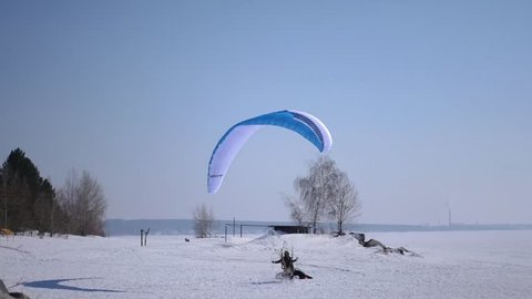 A man on a paraglider lands on the snow on a blue parachute. 4k. 3840x2160