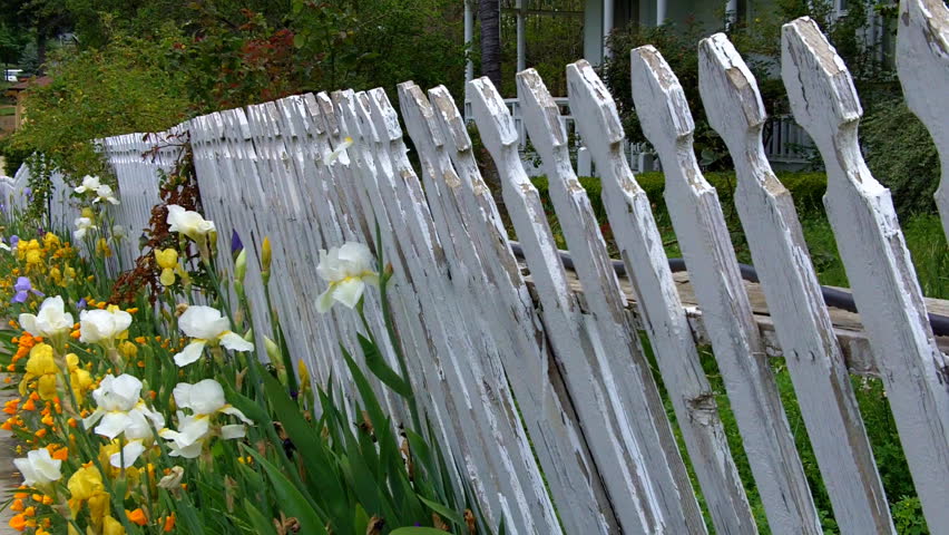 An old white picket fence with peeling paint and flowers nearby evokes small