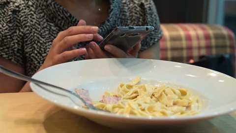 Woman using cell while having dinner with carbonara in Italian cafe