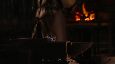 Blacksmith brings dripping hot metal from furnace and creates a shower of sparks as he beats a piece of white hot metal with a hammer on an anvil. Close up recorded.