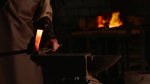 Blacksmith brings dripping hot metal from furnace and creates a shower of sparks as he beats a piece of white hot metal with a hammer on an anvil. Close up recorded.