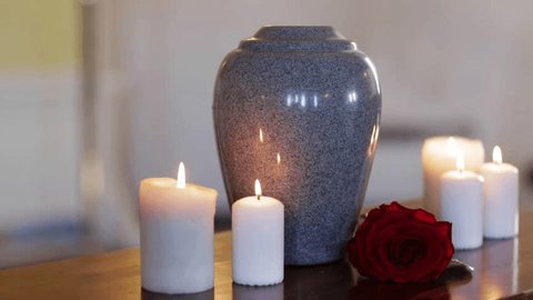 funeral, cremation, mourning and burial concept - funerary urn and candles on table burning indoors