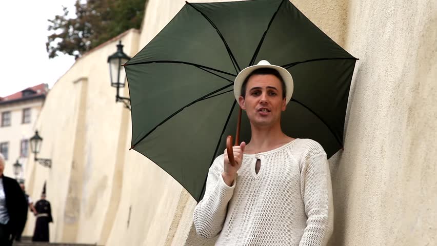 Young handsome man with umbrella is singing in Prague on a street
