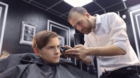 The bearded Barber cuts a little boy in the barbershop.
