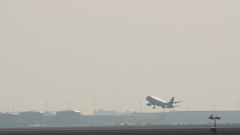 Amsterdam, March 2017. Airplane taking off from runway in hazy, sunny sky. Camera tracks with long lens.
