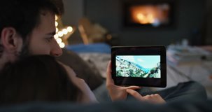 Closeup of couple using digital tablet by fireplace viewing travel photos on touchscreen browsing social media sharing wanderlust