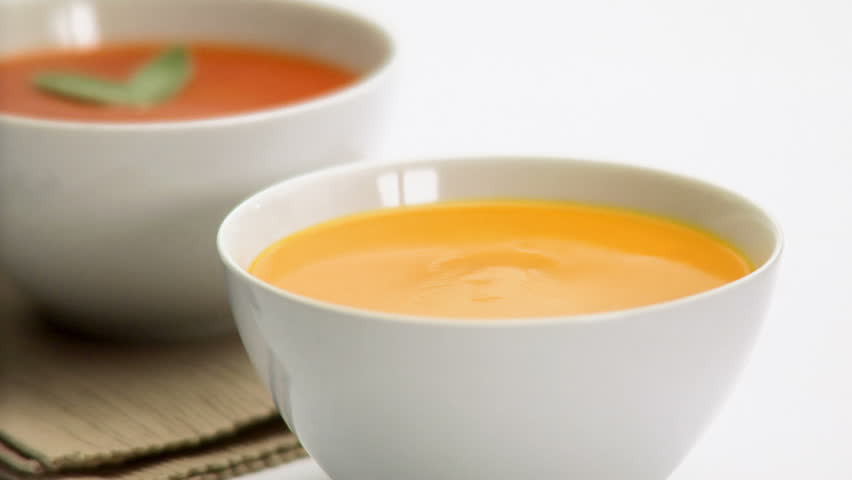 Chef garnishes butternut squash soup next to a red bowl of soup