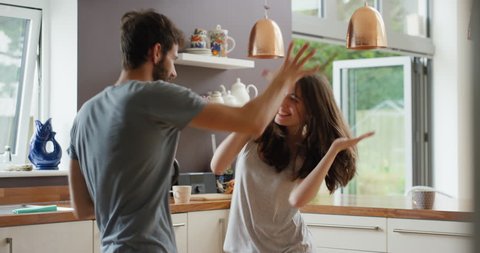 Happy young couple dancing in kitchen wearing pajamas listening to music morning at home