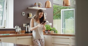 Young woman having video chat at home in kitchen holding smartphone blowing kiss at webcam chatting to friend