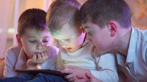 Three kids using tablet pc at home at night. Brothers with tablet computer in dark room. Children, boys playing games on tablet computer, emotions. Bedtime. Playing computer games, 4K UHD 3840x2160